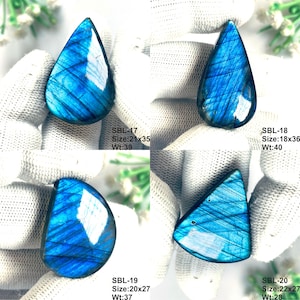 Pu&ograve; includere: Quattro pietre preziose di labradorite lucida con iridescenza blu. SBL-17 misura 21x35mm a 39ct, SBL-18 18x36mm a 40ct, SBL-19 20x27mm a 37ct e SBL-20 22x27mm a 28ct. Ogni pietra mostra una forma distinta e un profondo riflesso blu.
