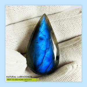 May include: A pear-shaped natural labradorite gemstone, displaying a striking blue iridescence. The stone is set against a white background. Text at the bottom reads "NATURAL LABRADORITE NEXT TO SEE MORE OPTIONS."