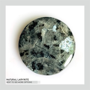 May include: A round, polished natural Larvikite stone with a speckled pattern of black and gray. The stone has a reflective, iridescent quality, with hints of blue and green. Text at the bottom reads: NATURAL LARVIKITE NEXT TO SEE MORE OPTIONS.