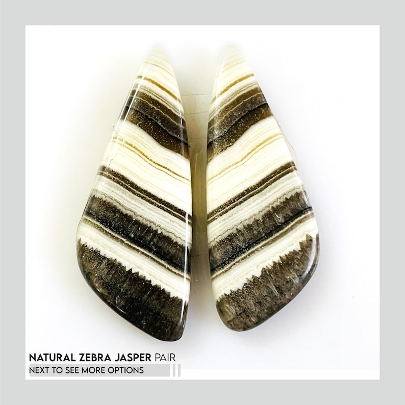 May include: Two polished zebra jasper stones. Each stone is a teardrop shape with alternating bands of white, tan, and dark brown. The stones are displayed on a white background. Text at the bottom reads "NATURAL ZEBRA JASPER PAIR" and "NEXT TO SEE MORE OPTIONS".