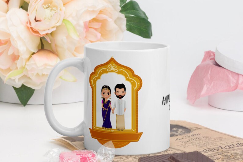 Puede incluir: Taza de cer&aacute;mica blanca con una ilustraci&oacute;n dorada de una pareja con ropa tradicional india. La pareja est&aacute; de pie en una puerta con un marco dorado. El texto "ANUJ & SHIVANI" est&aacute; impreso en la taza.