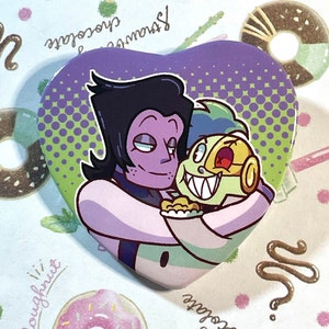 May include: Heart-shaped button featuring two cartoon characters in a loving embrace. The button has a purple background with a green and purple dotted design. The characters are in shades of purple, green, and yellow.