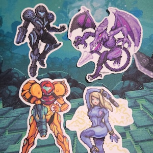 May include: Four pixel art stickers featuring characters from the Metroid video game series. The stickers depict Samus Aran in her various suits, and the antagonist Ridley. The stickers are in shades of purple, orange, and blue.