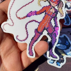 Pode incluir: Um adesivo de pixel art de uma personagem feminina em um macac&atilde;o vermelho com um chicote. Ela tem cabelo loiro e uma m&aacute;scara vermelha. O adesivo est&aacute; em um fundo branco.