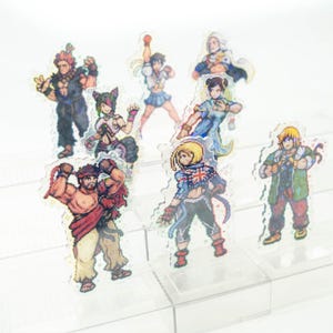 May include: A set of eight colorful cartoon character figurines, each standing on a clear acrylic base. The figurines are arranged on a three-tiered acrylic display stand.