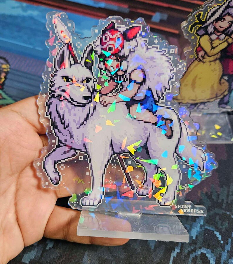 K&ouml;nnte beinhalten: Ein holografischer Acryl-St&auml;nder mit einem Pixelbild eines wei&szlig;en Wolfes, auf dem eine Person reitet. Die Person tr&auml;gt eine rote Maske und ein blaues und wei&szlig;es Outfit. Der St&auml;nder hat eine klare Basis mit dem aufgedruckten Text "SHINY SEABASS".