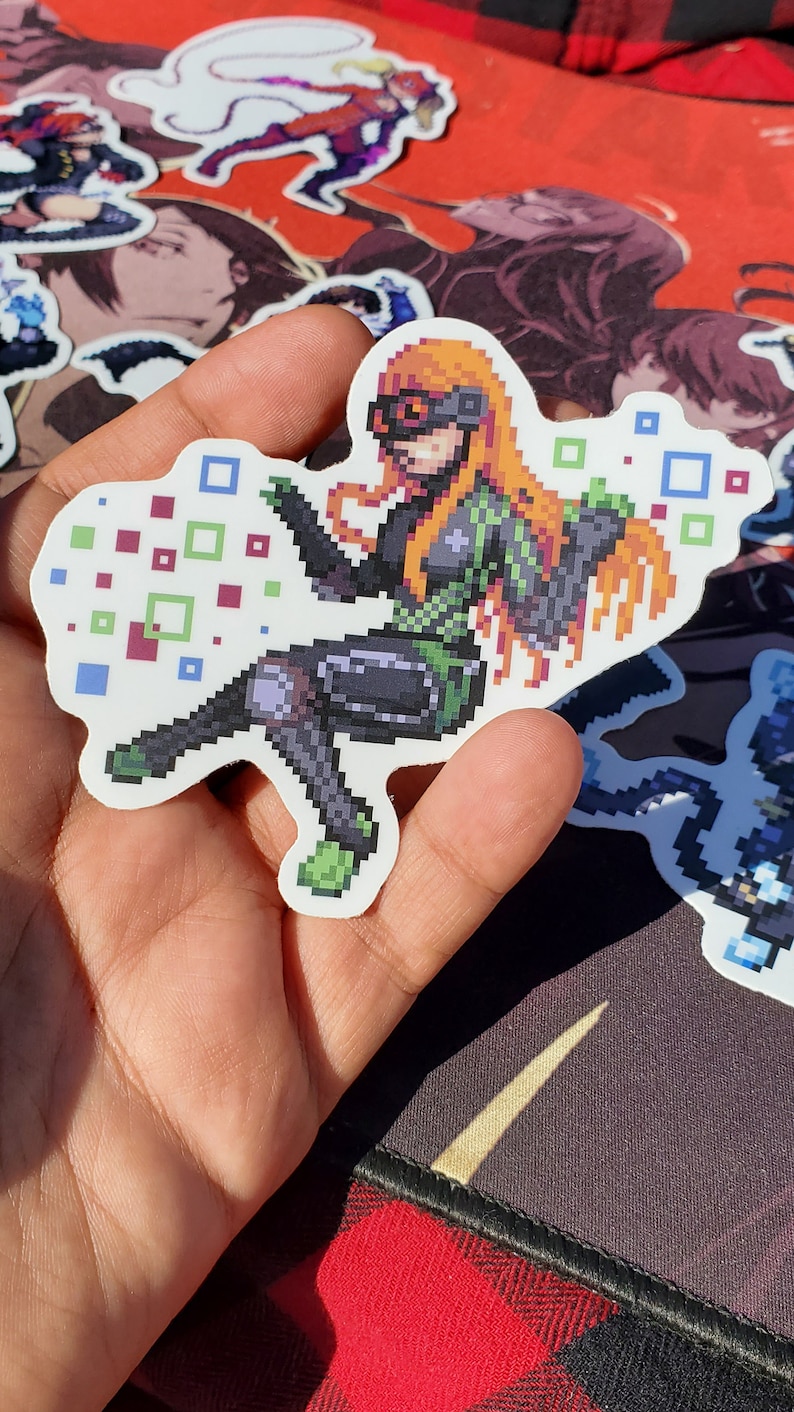 Pode incluir: Um adesivo de pixel art de uma personagem feminina com cabelo laranja, vestindo uma roupa verde e preta, sentada de pernas cruzadas e cercada por quadrados coloridos.
