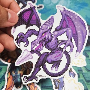 May include: A pixelated sticker featuring a purple dragon-like creature with large wings and a long tail. The sticker has a white border and the text "SHINY SEABASS" is visible. Other stickers are in the background.