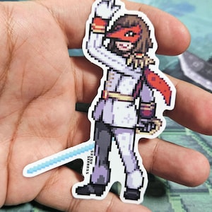 Pode incluir: Um adesivo de pixel art de um personagem vestindo uma roupa branca e vermelha com uma m&aacute;scara vermelha. O personagem est&aacute; segurando uma espada azul e tem uma capa vermelha. O adesivo est&aacute; em uma m&atilde;o.