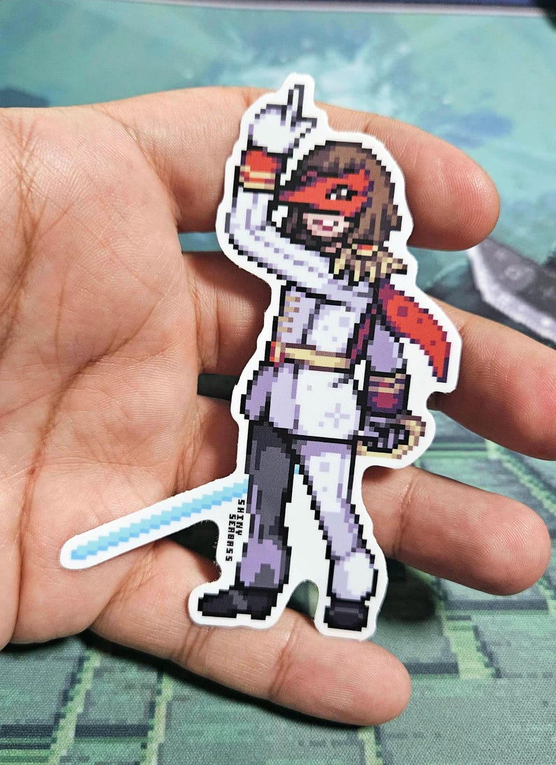 Pode incluir: Um adesivo de pixel art de um personagem vestindo uma roupa branca e vermelha com uma m&aacute;scara vermelha. O personagem est&aacute; segurando uma espada azul e tem uma capa vermelha. O adesivo est&aacute; em uma m&atilde;o.