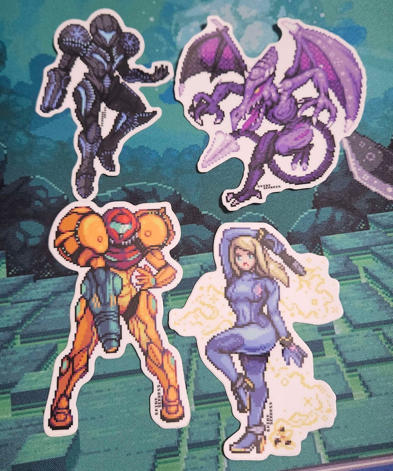 May include: Four pixel art stickers featuring characters from the Metroid video game series. The stickers depict Samus Aran in her various suits, and the antagonist Ridley. The stickers are in shades of purple, orange, and blue.