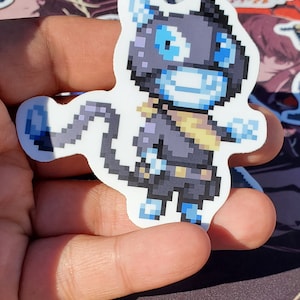 Pode incluir: Um adesivo de arte de pixel preto e azul de uma criatura semelhante a um gato com um cachecol amarelo. A criatura tem um rosto azul com olhos brancos e um largo sorriso.