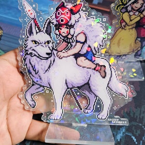 K&ouml;nnte beinhalten: Ein transparenter Acryl-St&auml;nder mit holografischem Finish zeigt eine pixelartige Illustration eines M&auml;dchens, das auf einem wei&szlig;en Wolf reitet. Das M&auml;dchen tr&auml;gt einen roten Hut mit wei&szlig;em Pelzbesatz und ein blaues Kleid. Der St&auml;nder hat einen wei&szlig;en Hintergrund mit glitzerndem Effekt. Der Text "SHINY SEABASS" ist auf der Unterseite des St&auml;nders aufgedruckt.