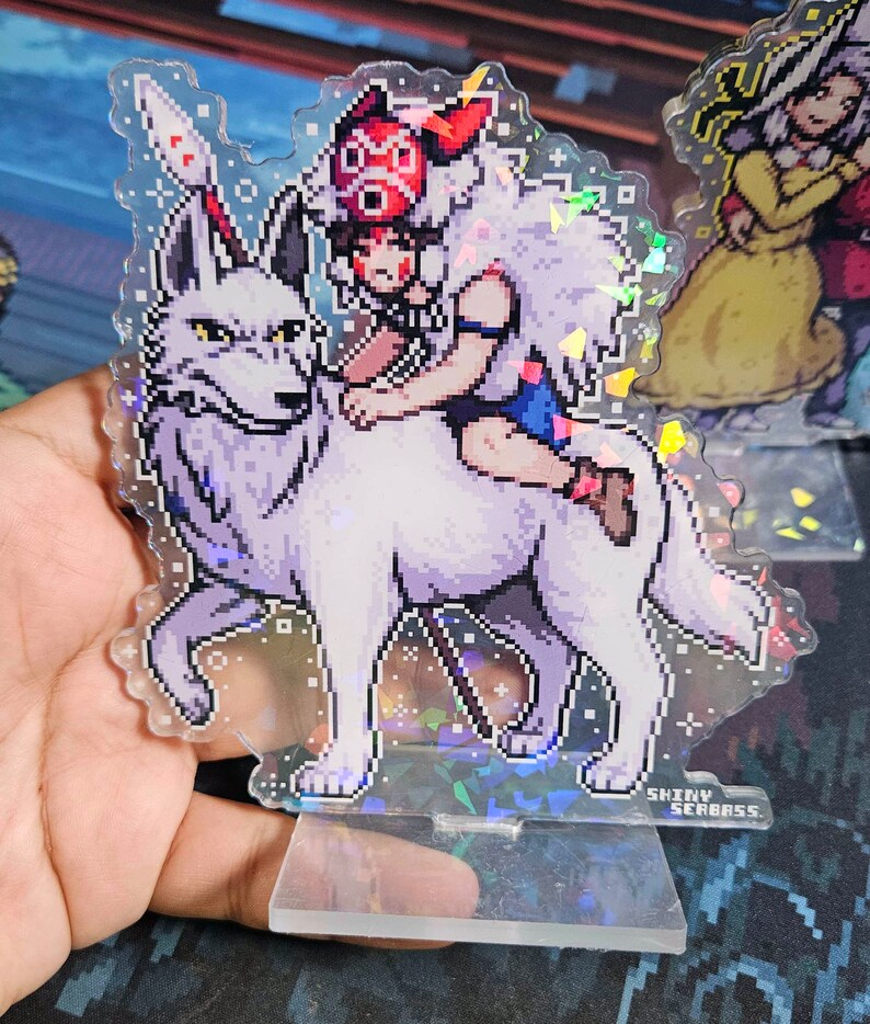 K&ouml;nnte beinhalten: Ein transparenter Acryl-St&auml;nder mit holografischem Finish zeigt eine pixelartige Illustration eines M&auml;dchens, das auf einem wei&szlig;en Wolf reitet. Das M&auml;dchen tr&auml;gt einen roten Hut mit wei&szlig;em Pelzbesatz und ein blaues Kleid. Der St&auml;nder hat einen wei&szlig;en Hintergrund mit glitzerndem Effekt. Der Text "SHINY SEABASS" ist auf der Unterseite des St&auml;nders aufgedruckt.