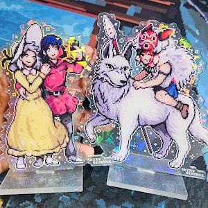 K&ouml;nnte beinhalten: Zwei Acryl-Charakter-St&auml;nder mit Anime-Charakteren. Der erste St&auml;nder zeigt zwei weibliche Charaktere, eine mit einem gelben Kleid und einem wei&szlig;en Hut und die andere mit einem roten Kleid. Der zweite St&auml;nder zeigt einen wei&szlig;en Wolf mit einem Charakter, der auf seinem R&uuml;cken reitet. Beide St&auml;nder haben eine glitzernde, irisierende Oberfl&auml;che und den Text "Shiny Seabass" auf der Unterseite.