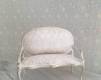 May include: A small, white, antique-style loveseat with a pink floral patterned fabric upholstery. The loveseat has a curved back and ornate legs.