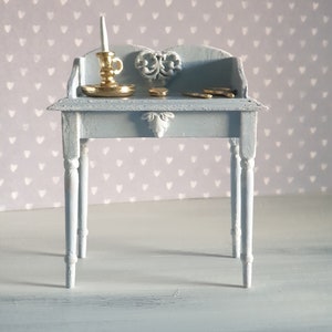 Könnte beinhalten: Ein hellblauer Holztisch mit einem geschnitzten Herzdesign auf der Oberseite. Der Tisch hat eine Schublade und vier Beine. Ein kleiner goldener Kerzenhalter mit einer weißen Kerze steht auf dem Tisch.