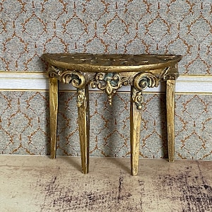 以下が含まれることがあります： 3本の脚を持つ、金色の装飾が施された三日月型のテーブル。テーブルは木製の彫刻が施されています。