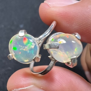 Puede incluir: Un anillo de plata con dos piedras preciosas de ópalo. Los ópalos son iridiscentes y tienen un color blanco, verde y rojo.
