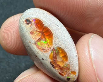 Op de afbeelding: Een witte opaal cabochon met oranje en groene flitsen van kleur. De opaal is gezet in een ruwe, natuurlijke matrix.