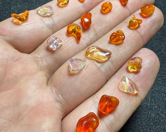 May include: A selection of small, polished gemstones in shades of orange, yellow, and iridescent colours. The gemstones are displayed on a hand, showcasing their varied shapes and textures. The image is well-lit, highlighting the stones' translucence.