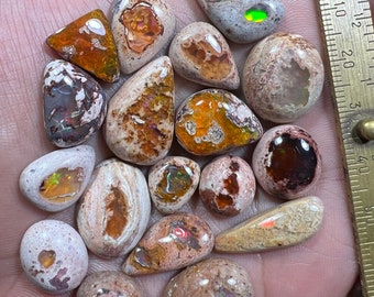May include: A collection of 17 natural opal cabochons in various shapes and sizes. The opals are a mix of white, brown, and grey with flashes of iridescent colour.