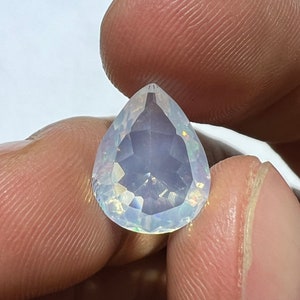 Puede incluir: Una piedra preciosa de ópalo facetada en forma de pera, transparente, con destellos iridiscentes de arcoíris.
