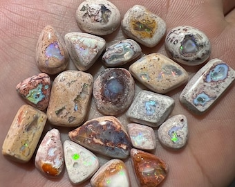 May include: A collection of 17 small, irregularly shaped opal stones. The stones are mostly white with brown and orange markings. Some of the stones have a rainbow sheen.