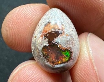 Peut inclure: Un cabochon d'opale en forme de larme avec une matrice blanche, grise et brune. L'opale présente un arc-en-ciel de couleurs, notamment le rouge, l'orange, le jaune, le vert, le bleu et le violet.