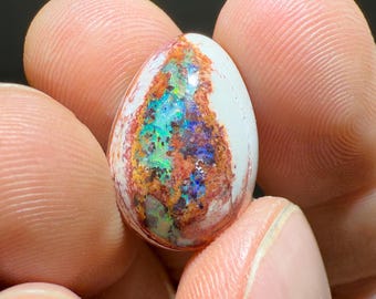Op de afbeelding: Een ovale opal cabochon in wit en bruin met iriserende blauwe, groene en rode flitsen. De opal is gezet in een heldere epoxy.