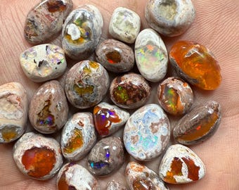 May include: A selection of polished opal gemstones in various shapes and sizes. The opals display a range of colours, including orange, white, brown, and iridescent flashes. Some stones have a speckled appearance, while others are smooth and rounded.