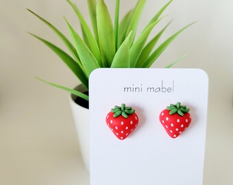 May include: A pair of red and green strawberry earrings on a white card with the text "mini mabel" and "www.minimabel.com".
