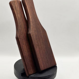 May include: Two wooden spatulas with dark brown handles and blades, standing upright on a black wooden base.