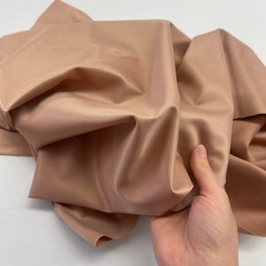 Könnte beinhalten: Nahaufnahme eines pfirsichfarbenen Stoffes mit einer dezenten Rippenstruktur. Der Stoff ist weich und fällt schön.