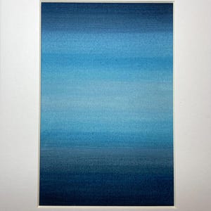 May include: Abstract art print with a gradient of blues, transitioning from dark navy to lighter tones. The artwork is mounted within a white mount, enhancing the visual impact. The piece creates a tranquil atmosphere, suitable for various interior settings.