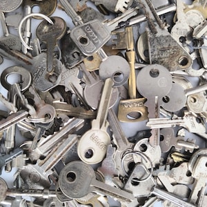 May include: A collection of various metal keys, some with key rings, scattered across a surface. The keys are in different shapes and sizes, with a mix of silver, gold, and tarnished finishes. The image is a close-up shot.