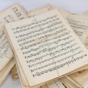 May include: A collection of vintage sheet music, with pages showing musical notation. The pages are tied together with twine. The paper has a yellowed, aged appearance, suggesting the music is old.