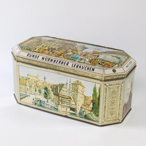 May include: A vintage tin box with a gold trim and a colourful illustration of a German city scene. The text on the box reads "Runde Nürnberger Lebkuchen".