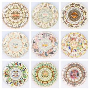 Könnte beinhalten: Neun dekorative Keramikteller mit bunten Designs mit Tieren, Vögeln und Blumenmustern. Jeder Teller hat einen Kalender für ein anderes Jahr, darunter 1975, 1976, 1981, 1988, 1989 und 1991.