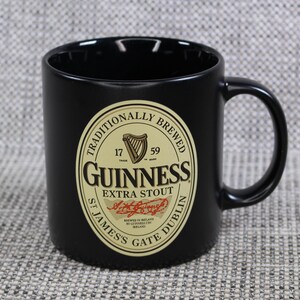 May include: Black ceramic Guinness mug with a large handle. The mug features the Guinness logo in gold and black, with the words "Guinness Extra Stout" and "St. James's Gate Dublin" printed on the front.