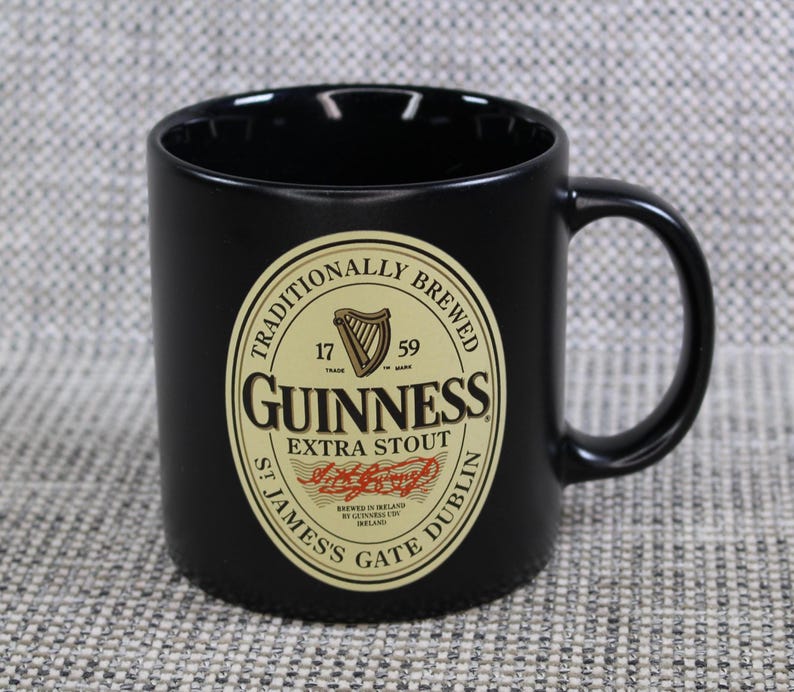 May include: Black ceramic Guinness mug with a large handle. The mug features the Guinness logo in gold and black, with the words "Guinness Extra Stout" and "St. James's Gate Dublin" printed on the front.