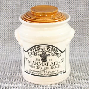 Può includere: Un barattolo di ceramica bianca con un coperchio marrone. Il barattolo ha un'etichetta nera che recita "A Royal Taste July 1981 Marmalade D with Drambuie Liqueur Commemorating the Wedding of HRH The Prince of Wales & Lady Diana Spencer".