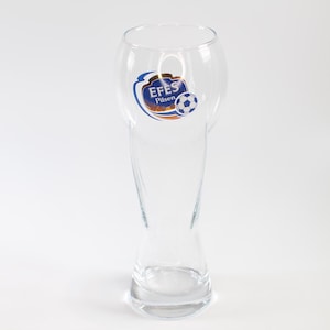 May include: A clear glass beer pilsner with a curved top and a slender body. The glass features a logo with the text "EFES Pilsen" and a soccer ball graphic. The glass is designed for beer and is set against a white background.