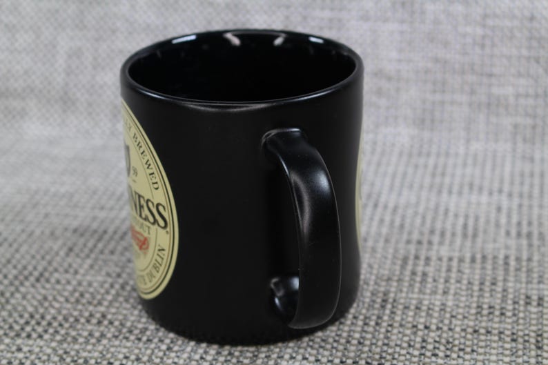 May include: Black ceramic mug with a curved handle. The mug features a circular label with the word "Guinness" and other text. The mug is designed for beverages and is suitable for home or office use.