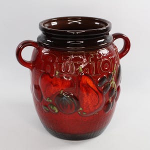 May include: A red ceramic jar with two handles and a dark brown rim. The jar is decorated with embossed fruit designs, including apples, pears, and grapes. The word "RUITOR" is embossed on the jar.