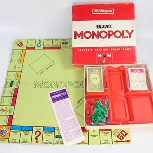 Könnte beinhalten: Ein Vintage Travel Monopoly Brettspiel-Set. Die rot-weiße Box trägt die Aufschrift "Waddingtons Travel Monopoly". Das Spielbrett ist hellgrün mit Grundstücksfeldern. Enthält Spielsteine, Karten und Anweisungen.