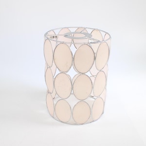 Op de afbeelding: Cilindrische lampenkap met een zilverkleurig metalen frame en lichtroze ovale panelen. De kap is ontworpen om licht te verspreiden en een decoratief element aan een lamp toe te voegen. Hoogte: ongeveer 20 cm.