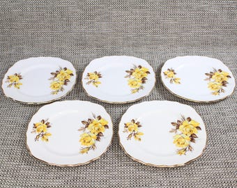 May include: Set of five white ceramic plates with a gold rim. Each plate features a yellow rose floral design.