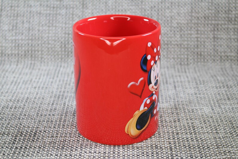 Peut inclure: Mug rouge en c&eacute;ramique avec Minnie Mouse. Le mug a une finition brillante et une forme cylindrique. Minnie Mouse est repr&eacute;sent&eacute;e dans sa tenue classique avec un n&oelig;ud &agrave; pois et des gants. Un c&oelig;ur est &eacute;galement en relief sur le mug.