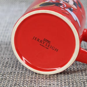 Peut inclure: Une tasse en c&eacute;ramique rouge avec un bord blanc et une anse rouge. Le fond de la tasse porte l'inscription "JERRY LEIGH" et le logo Disney. La tasse pr&eacute;sente un motif de dessin anim&eacute; sur le c&ocirc;t&eacute;.